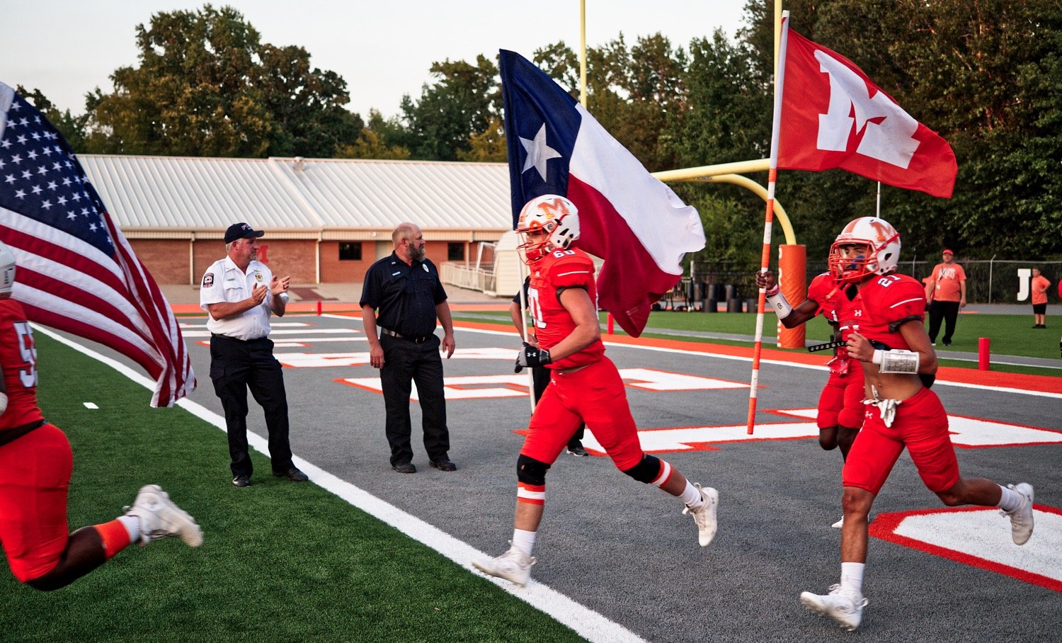 Javaryon Brumsey, Tanner Crenshaw and JaMarcus Kennedy carry the American, Texan and Mineola flags, respectively, through the welcome first-responders before action against West Rusk on Friday.